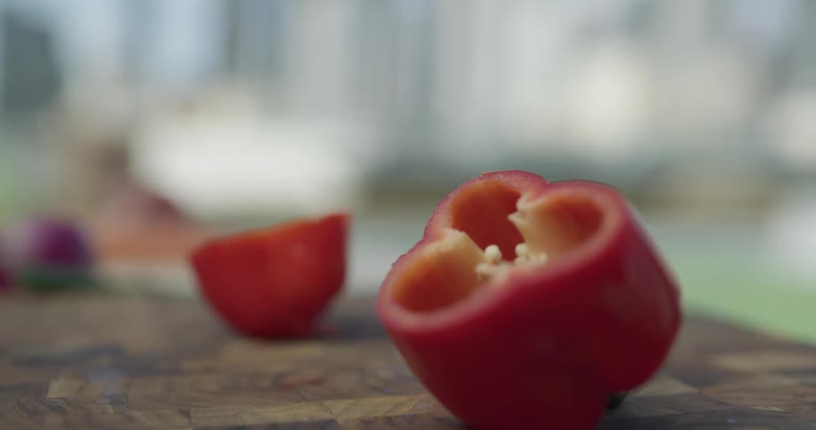 A chef violently chops a red bell pepper on a wooden chopping board