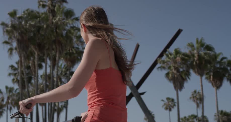 Woman rides a bike past palm trees on a sunny day