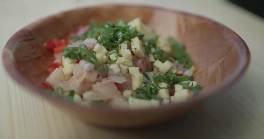 Someone sprinkles seasoning onto food in a wooden bowl