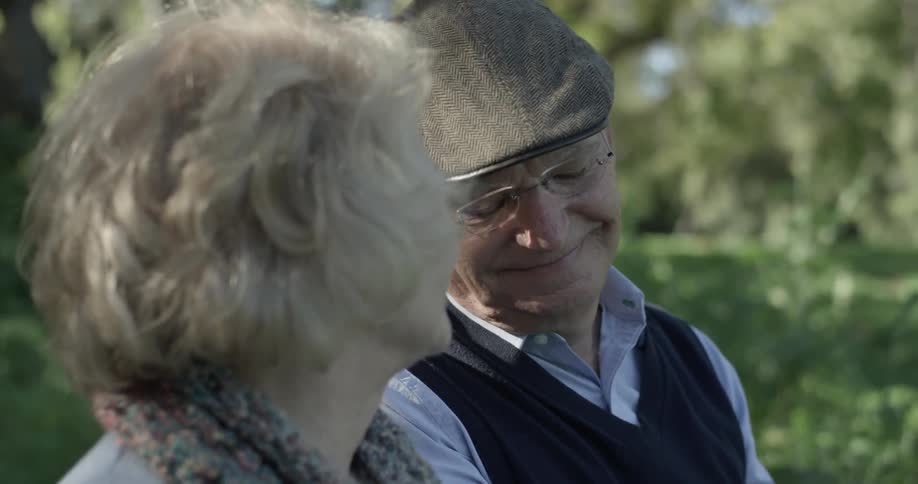 A man looks down at the hands of a woman and looks up at her to smile at her while she smiles back at him