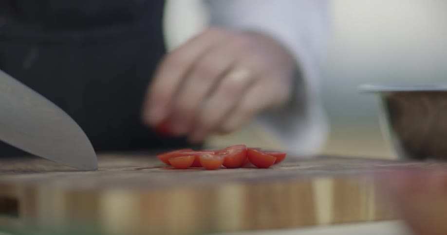 A chef chops up tiny small tomatoes on a cutting board and then scoops them up