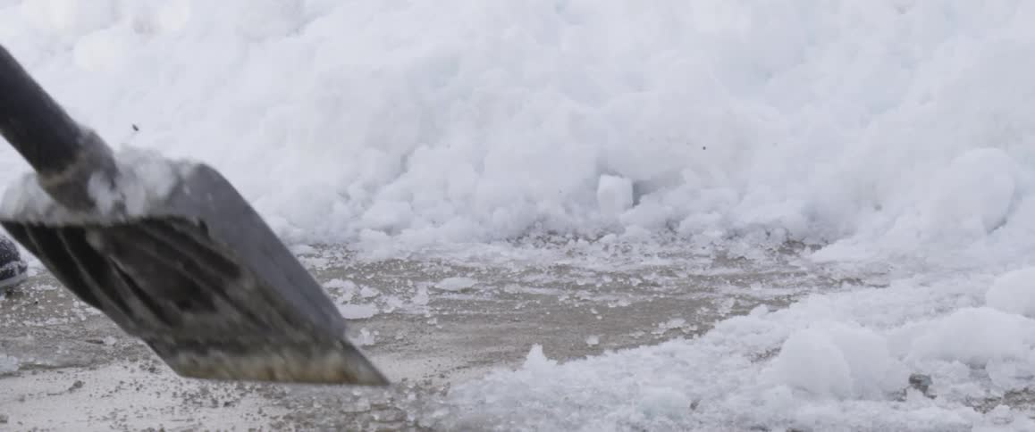 A person shoveling icy snow off of pavement