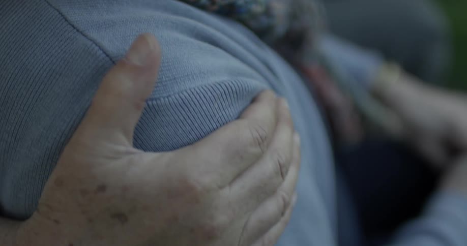 An elderly man grasps the shoulder of an elderly women and rubs her shoulder to comfort or sooth her