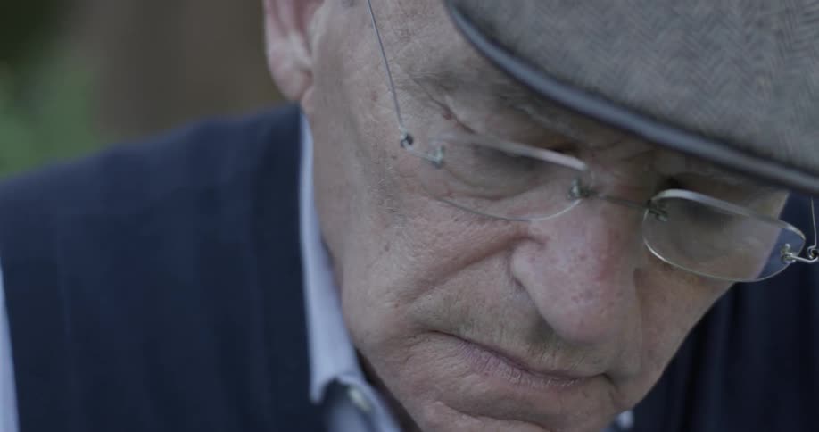 A seated older male looks down in thought
