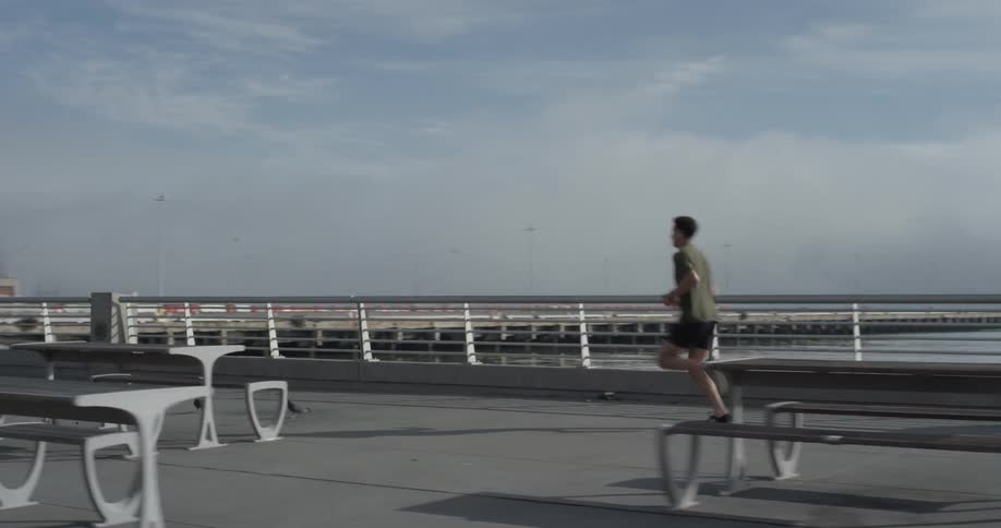 Man jogs along pier with picnic tables