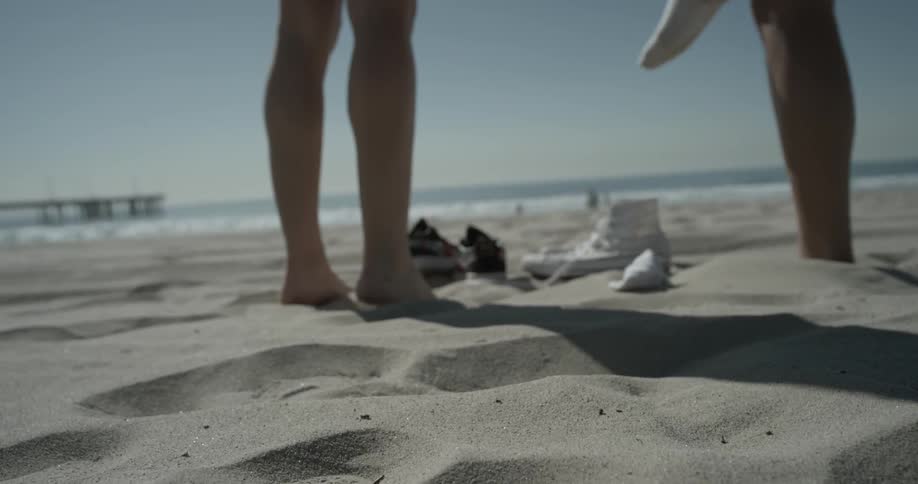 Two young women removing their socks and shoes on the beach