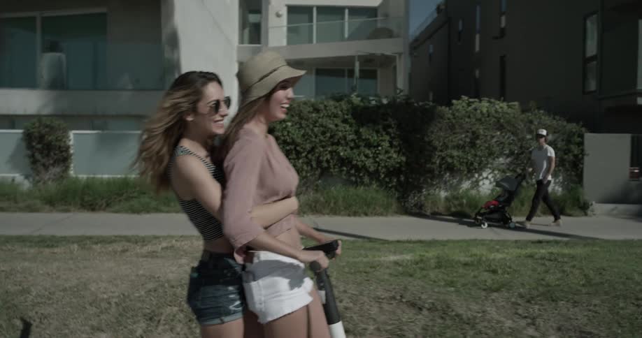 Two women ride a scooter down the road during the day