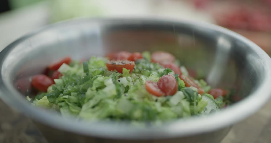 A bowl of lettuce and tomatoes getting the final touches of seasoning as a chef throws pepper into the bowl