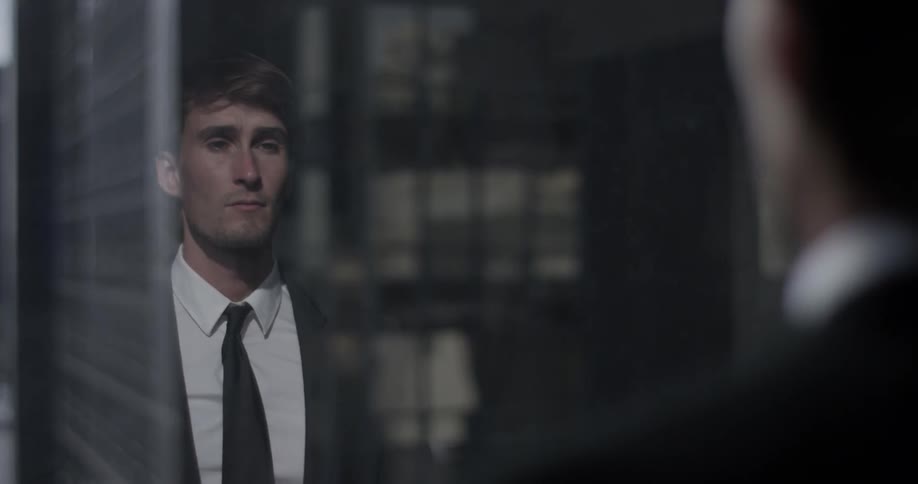 A man suits up in front of a window overlooking the city buildings