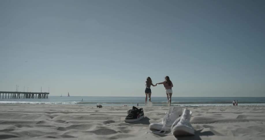 A pair of women running down the beach into the ocean
