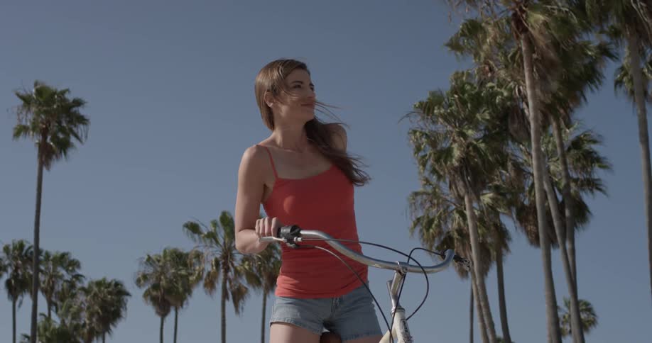 A woman looks at a phone as she sits on a bike near palm trees