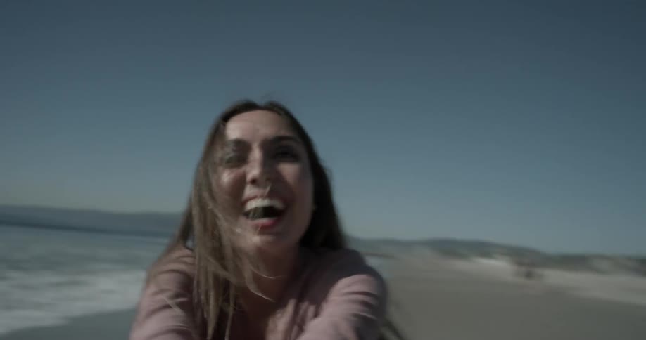 Woman laughs and spins in circles on beach in the afternoon