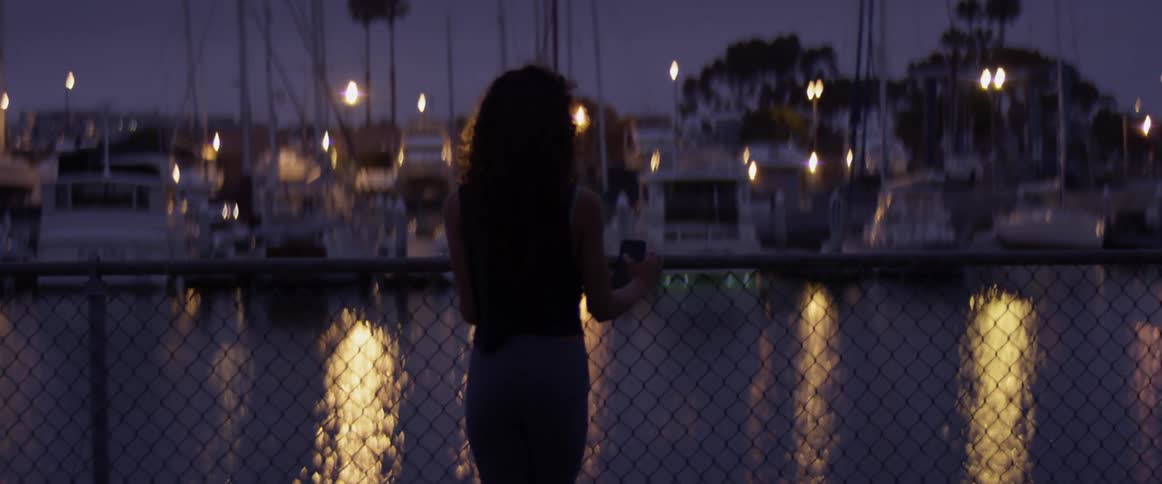 Woman leaning over a fence to look at boats at night