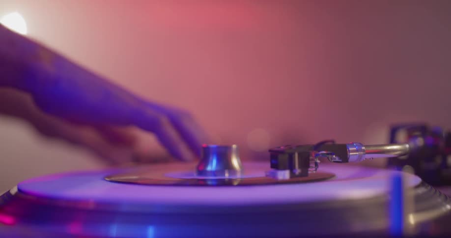 A man is scratching a record on a record playing mixing and rewinding it to make music for the concert he is playing on stage