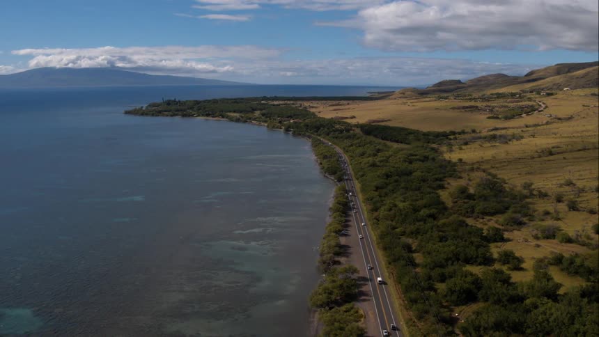 Cars pass along road that borders a body of water