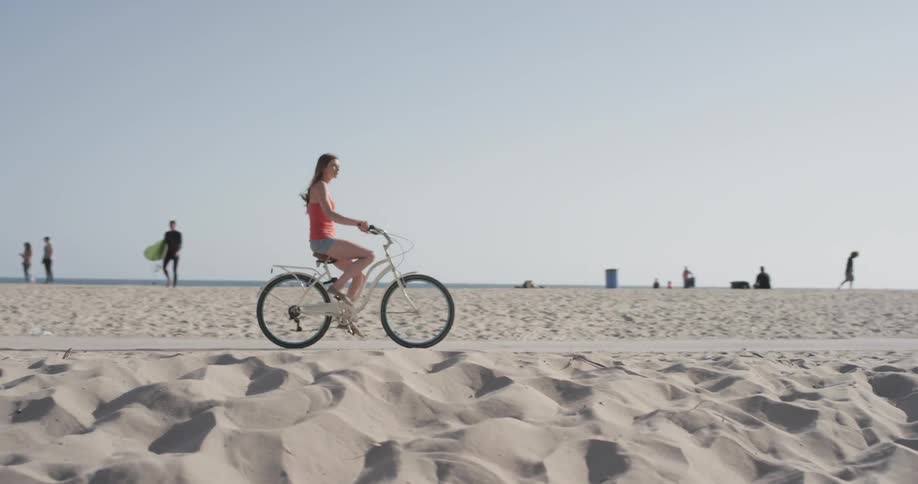 Woman rides a bikes on a sidewalk on the beach
