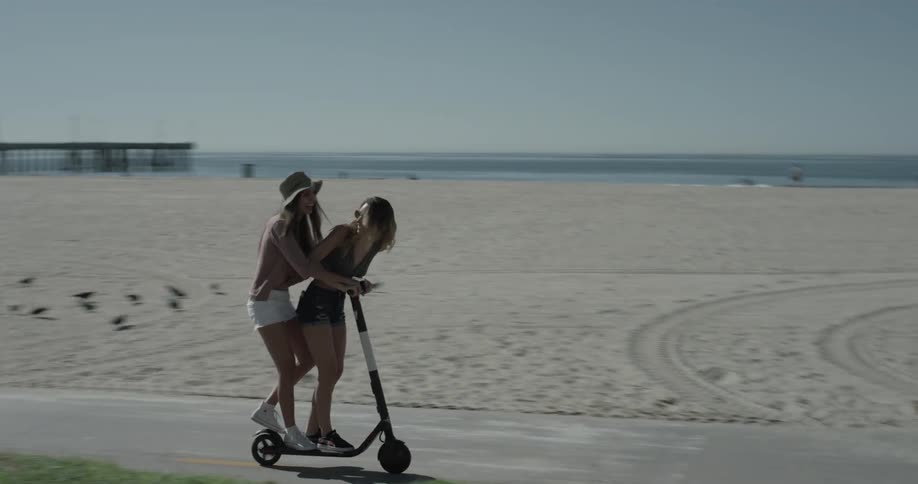 Two woman are on a scooter by the beach