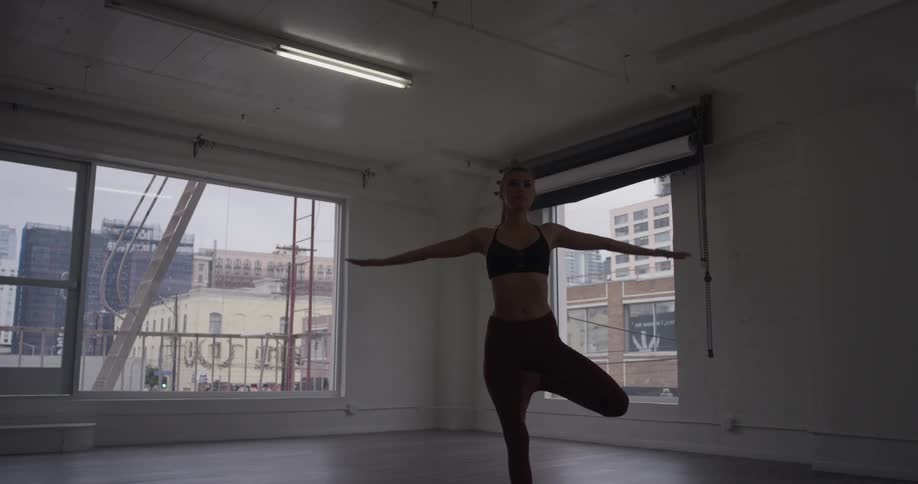 A woman in yoga pants and bra standing on one leg and posing with her arms in the air