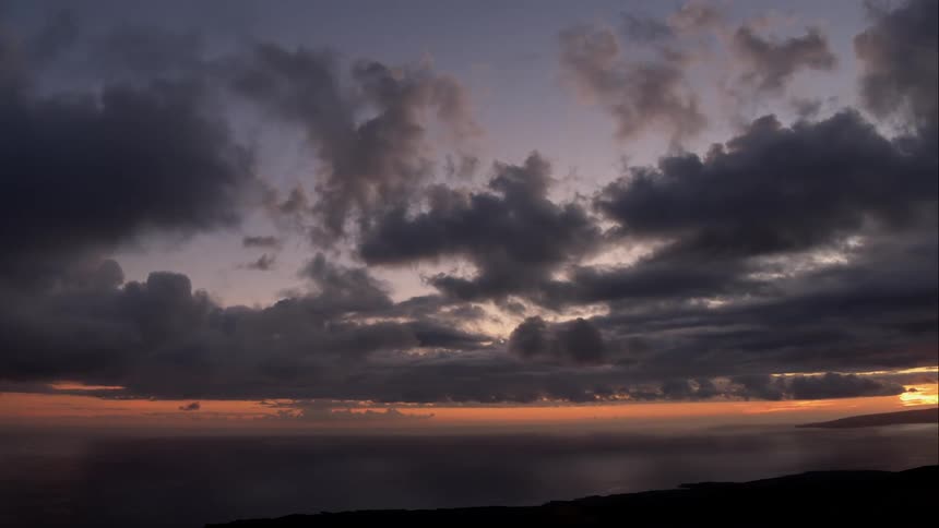The sun sets beneath a cloudy sky over the water