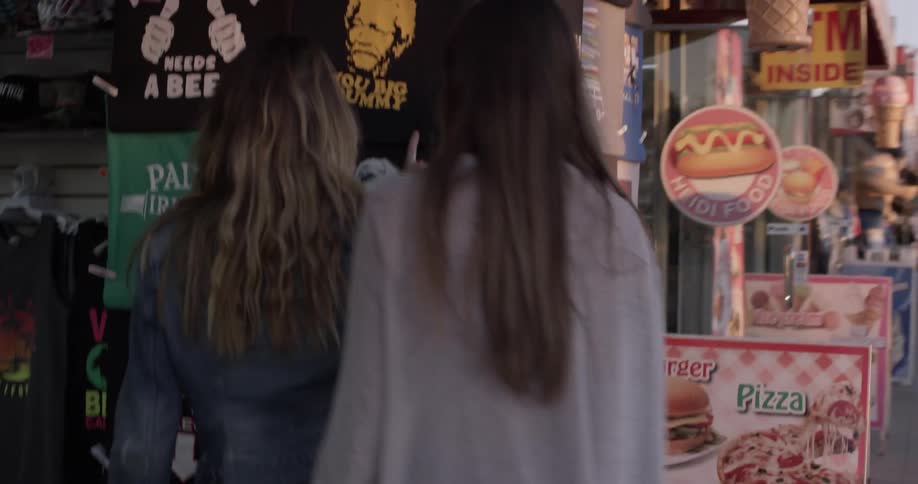 Two woman are looking at shirts outside on the store wall