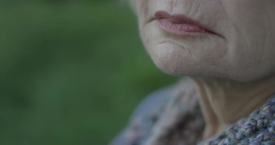 An old woman peers blankly into the distance as she sits outside