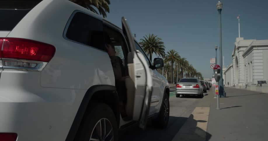 A man talking on a cell phone gets out of a car