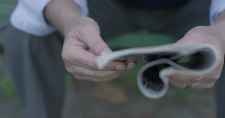 A man on a park bench holds a newspaper in his hands and is reading