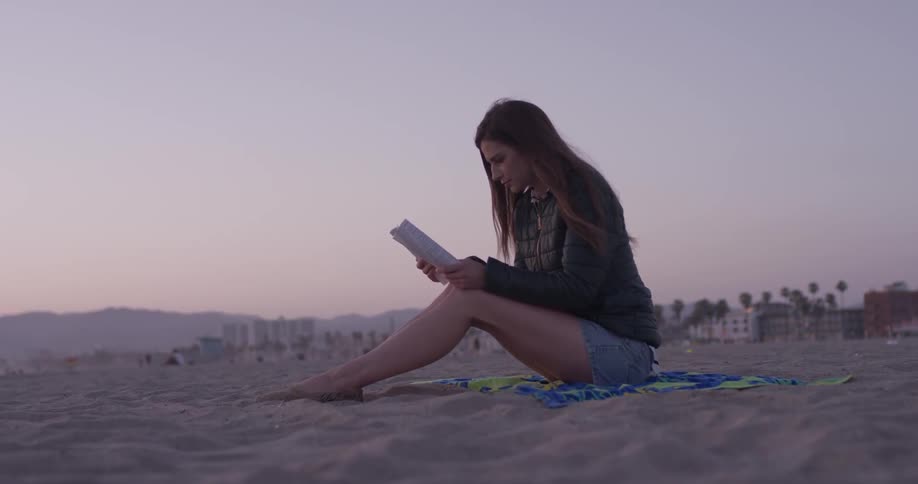A woman is sitting on a towel on the sand