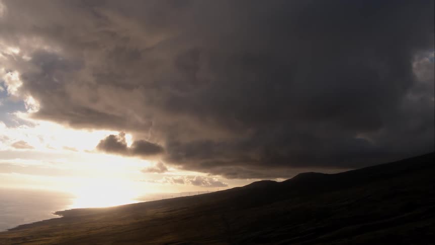 A very large storm cloud over hills near an ocean