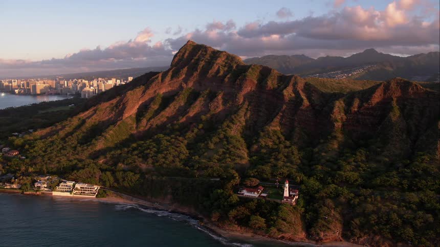 A mountain rises up from the ocean with a building on the beach below it