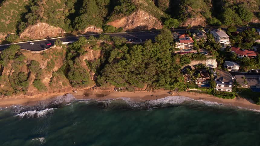 Waves breaking on the beach near large houses and a highway