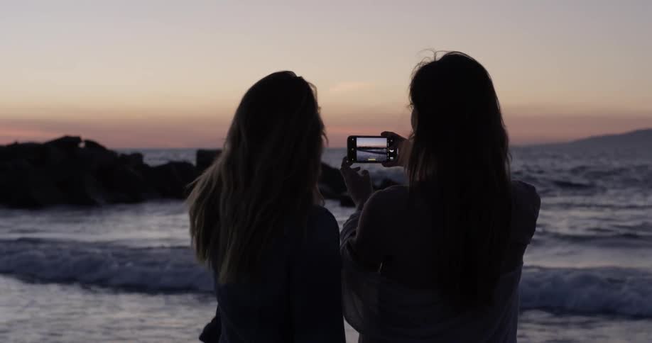 Two females record the ocean at dusk