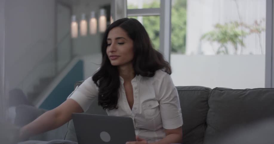 A woman sitting on the couch with her laptop and drinking out of a coffee mug