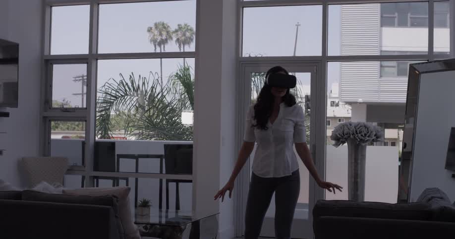 A woman putting on virtual reality glasses while standing in an upscale apartment