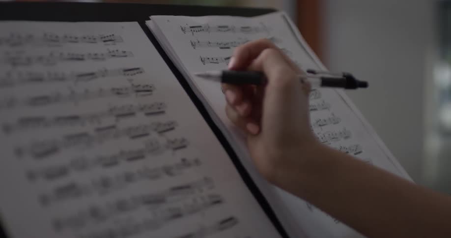 Woman holds a pen and moves sheet music around on a holder and makes corrections and circles notes on the paper