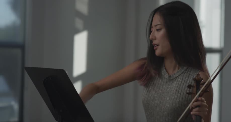 Woman is playing violin and gets upset and throws the sheet music off of the sheet music holder on a bright sunny day indoors