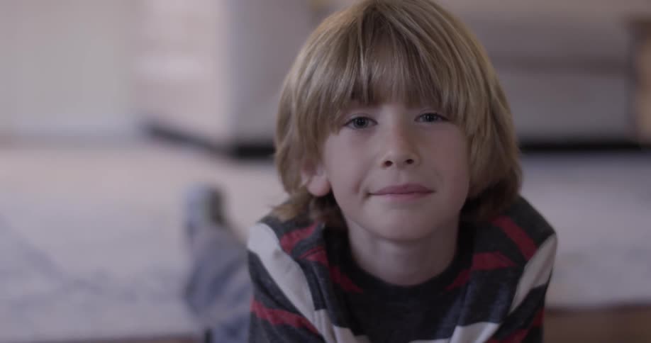 Boy looks at drawing while laying on stomach on floor