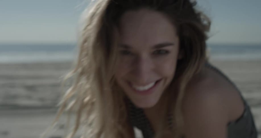 A woman smiles and sprinkles sand from her hands on the beach
