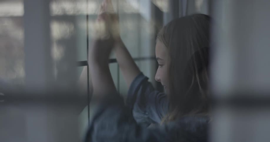 A young girl presses her hands to a window at someone on the other side