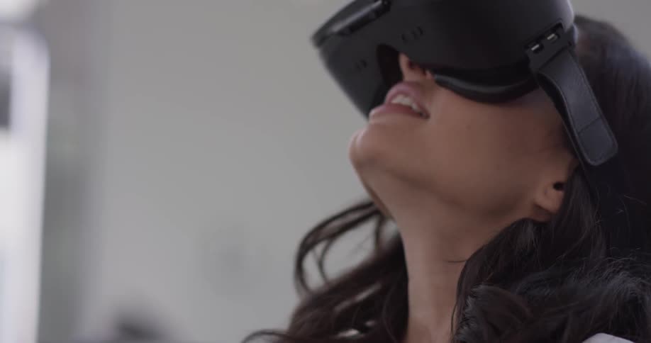 A woman has virtual reality goggles on and seems to be interested in the experience as she looks around