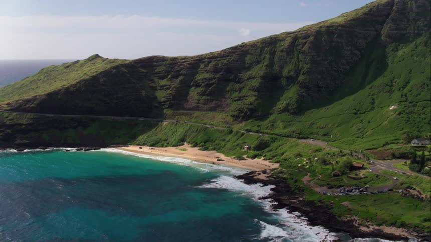 Blue green water surges against beach backed by green hills