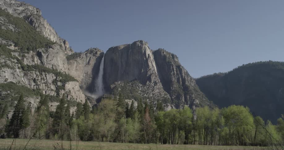 A view of a field with a rocky cliff and waterfall behind it on a sunny day