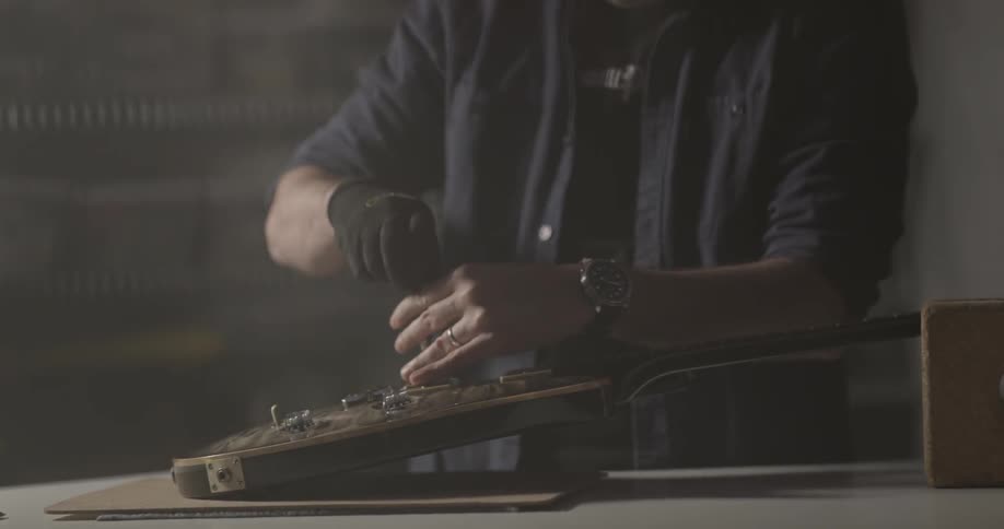 Man unscrews the picks ups of an electric guitar in a dim lit room of his garage and opens a package