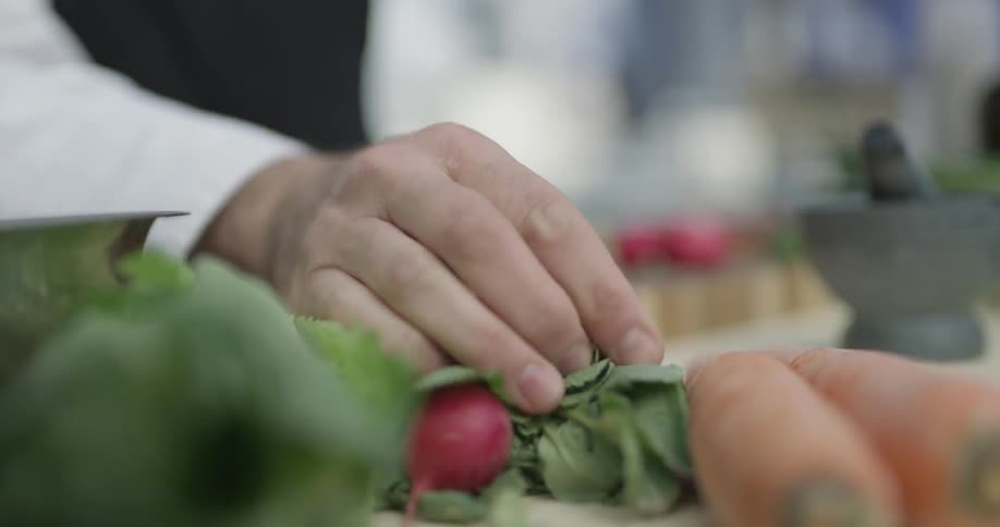 A chef picks some radishes up and bring them to a cutting board to chop and prep