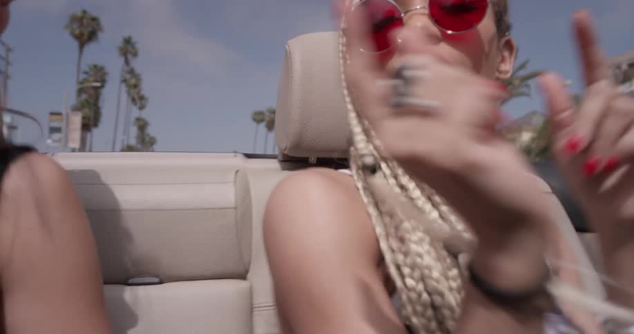 Two women ride in a convertible dancing and singing