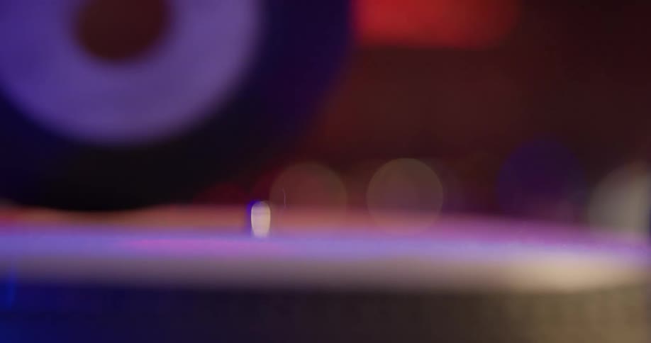 A record is taken off of a record player by a dj in a red and blue lit room