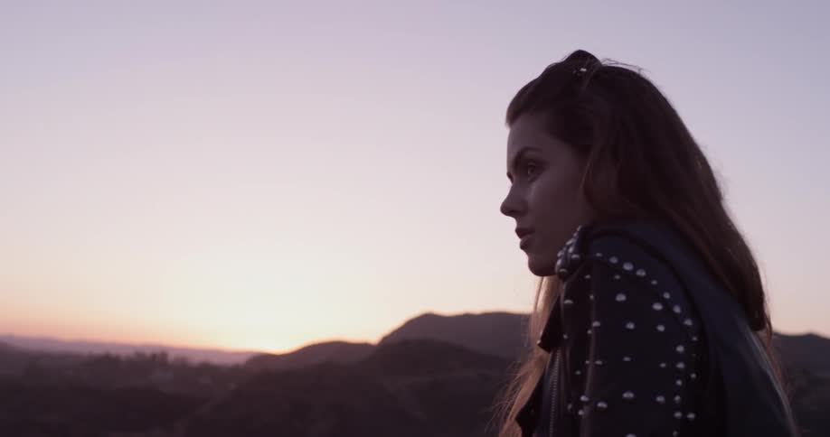 Woman in a leather jacket looking out over a valley and breathing in deep