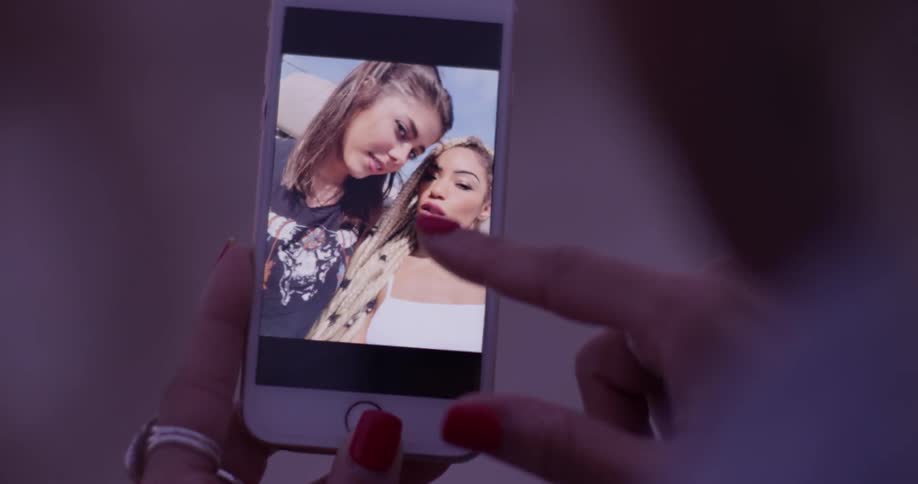 Two women looks through pictures on a cellphone they took together of each other selfies rather and the sun seems to have set
