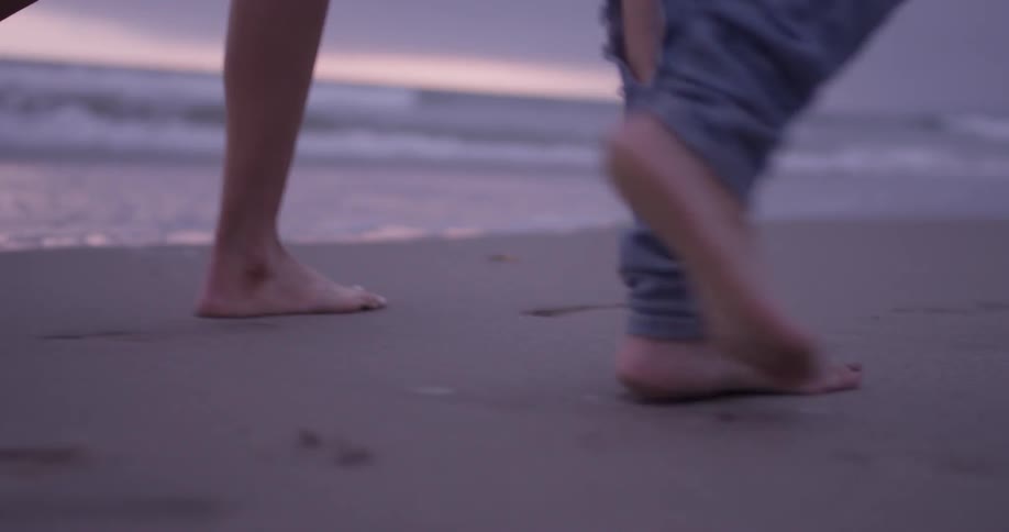 Two women walk barefoot along a beach