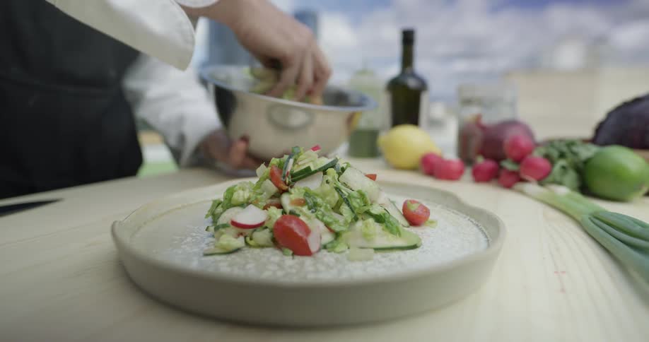 A chef removes a mixture of chopped vegetables from a mixing bowl using their hands